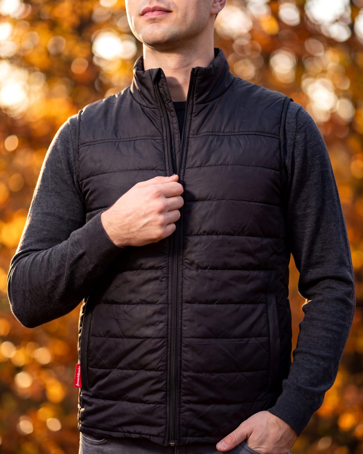 Un homme en plein air en automne remonte la fermeture éclair d'une veste matelassée heatlover noire.
